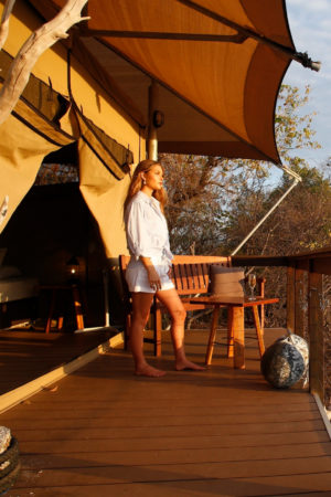 A girl stands with a glass of wine in hand, admiring the beautiful Cygnet Bay and remote location that surrounds her Glamping Safari Tent in the Diver's Village of Cygnet Bay Pearl Farm.