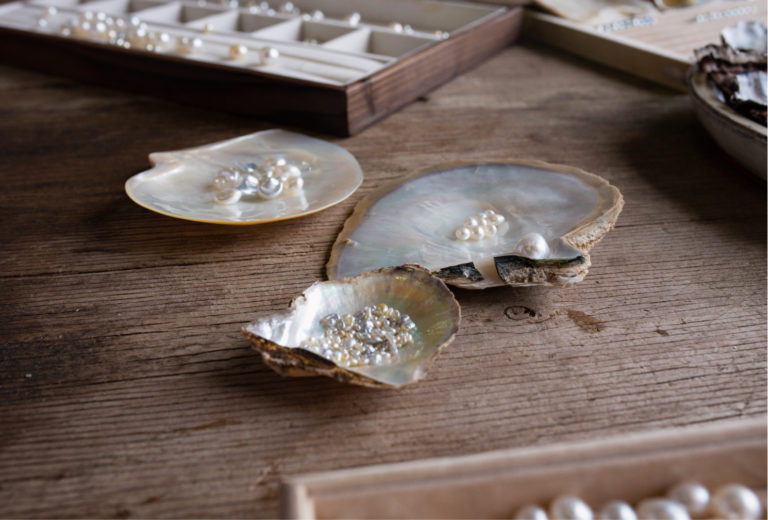 Three mother of pearl shells sit on a wooden table. In one shell are Australian South Sea pearls grown at our Cygnet Bay Pearl Farm. In the other shell are Australian Akoya pearls grown at our Broken Bay Pearl Farm. In the Akoya mother of pearl shell are Australian Akoya Keshi pearls also grown at Broken Bay Pearl Farm. Guests are encouraged to touch and feel these pearls during our Shellar Door Pearl Grading Experience. How Do You Tell if Pearls are Real?