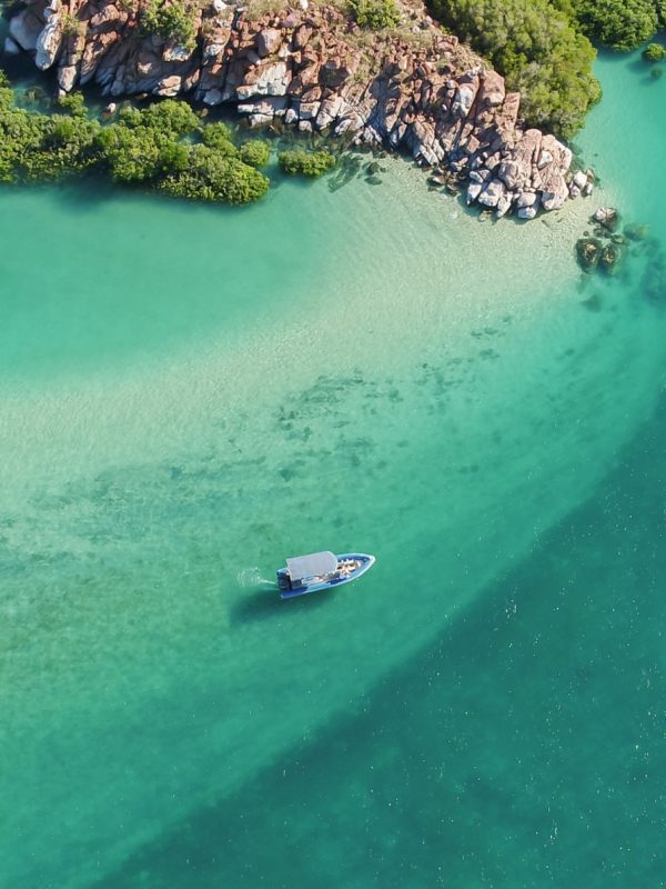 A beautiful aerial visual of a boat dancing across the waves, travelling past the Archipelago Islands that are scattered along the coastline of the Dampier Peninsula, with turquoise blue waters that are almost crystal clear.
