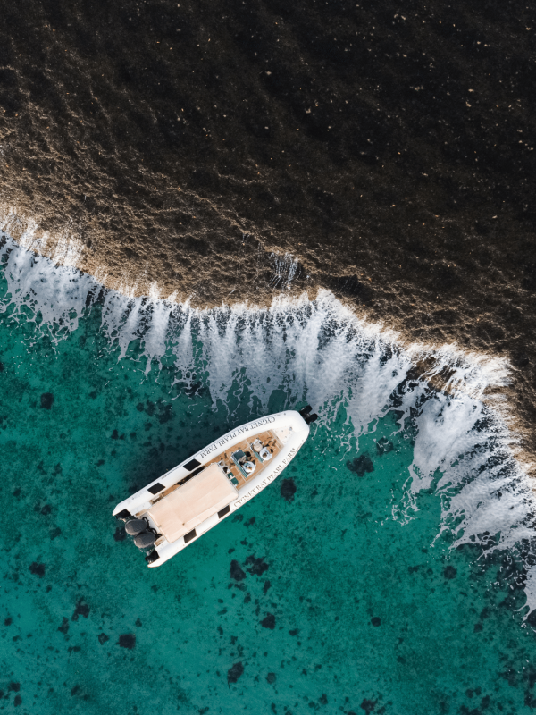 A Cygnet Bay boat sits idly next to the iconic Waterfall Reef, spilling water during the low tide of the ocean. The guests on the boat bare witness to this unique natural phenomenon and are in awe of it's cascading waterfall effect.