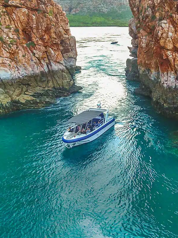 A boat sits on the calm, turquoise waters in the foreground, in front of the iconic Horizontal Falls. The Horizontal Falls are an unusual natural phenomenon on the coast of the Kimberley region in Western Australia, where tidal flows causes waterfalls on the ebb and flow of each tide.