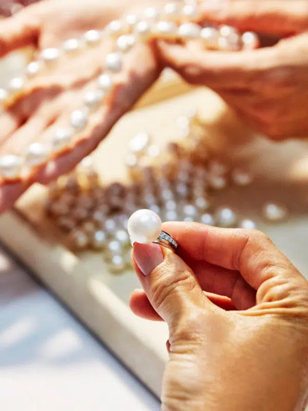A customer holds a beautiful Australian South Sea pearl ring, that is surrounded by white diamonds within the band of the ring. In the background a customer service person holds a lustrous Keshi pearl strand, featuring Australian South Sea Keshi pearls grown at our very own Cygnet Bay Pearl Farm.