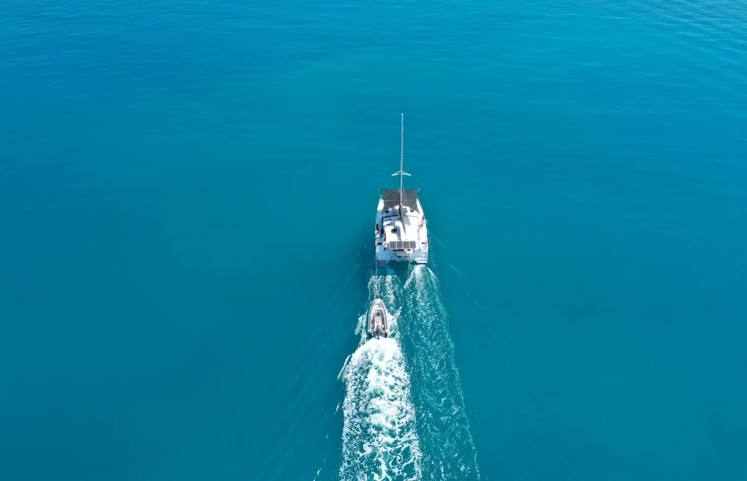 A boat with a tender in tow travels along the calm, blue Broome waters with guests enjoying the beautiful sights of the Kimberley.