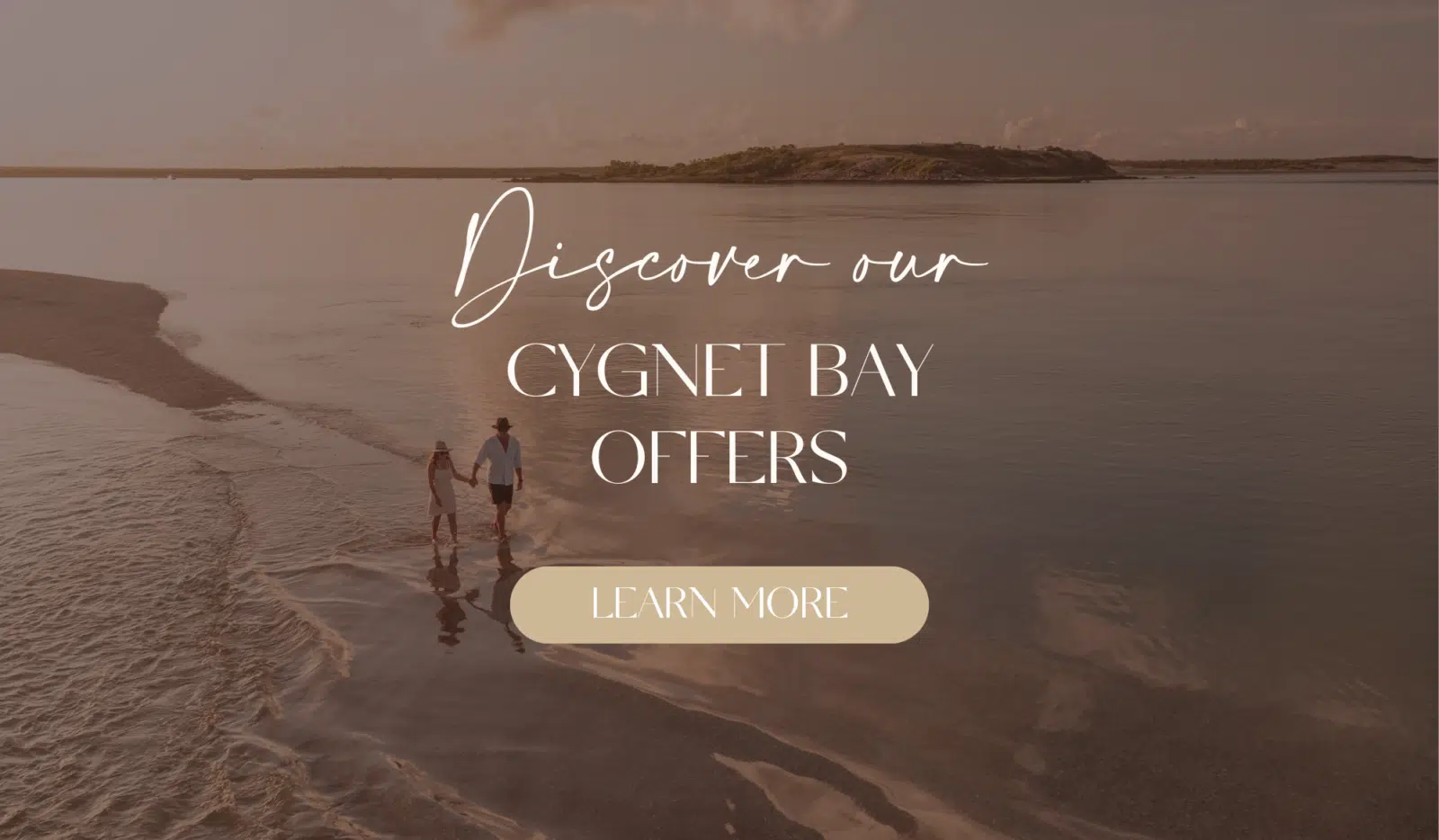 A couple walk hand in hand at sunset on the shoreline of a secret island. The sea is so still that it reflects that couple, the beautiful white clouds, and the peachy tones of the sunset. In the distance is the coastline of the Dampier Peninsula, with sandy white beaches.
