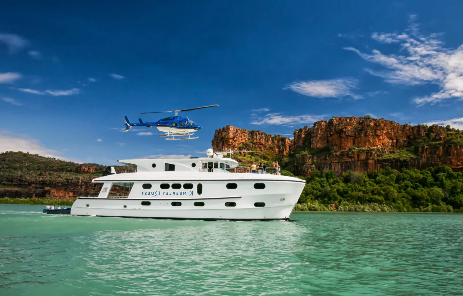 A helicopter lands on the Kimberley Quest, with Mitchell Falls in the background and the beautiful turquoise waters in the foreground.