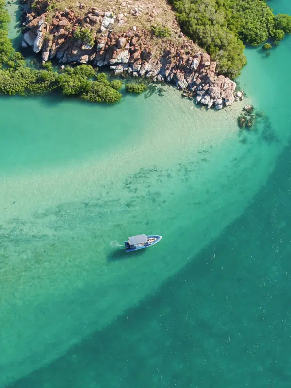 A beautiful aerial visual of a boat dancing across the waves, travelling past the Archipelago Islands that are scattered along the coastline of the Dampier Peninsula, with turquoise blue waters that are almost crystal clear.