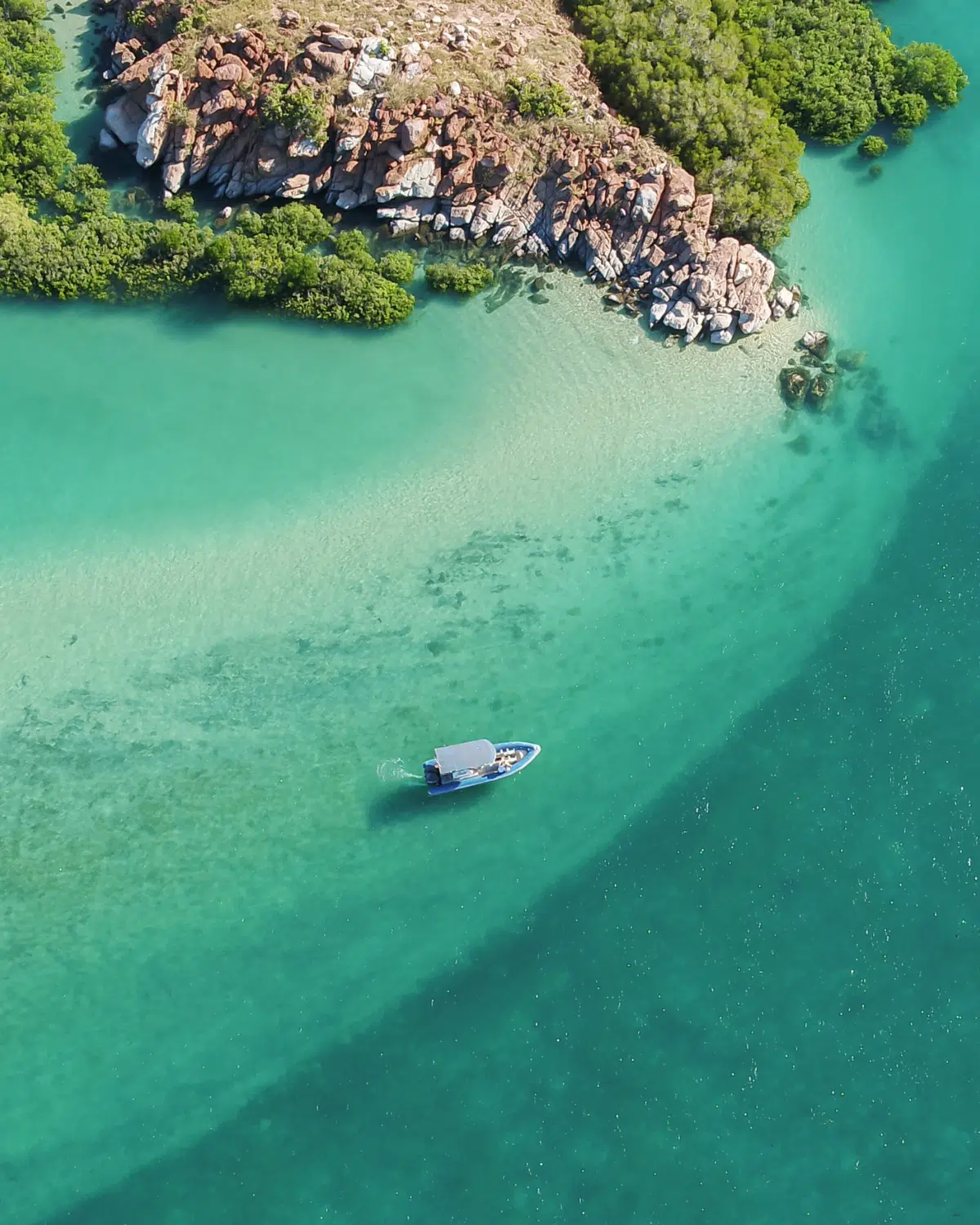 A beautiful aerial visual of a boat dancing across the waves, travelling past the Archipelago Islands that are scattered along the coastline of the Dampier Peninsula, with turquoise blue waters that are almost crystal clear.