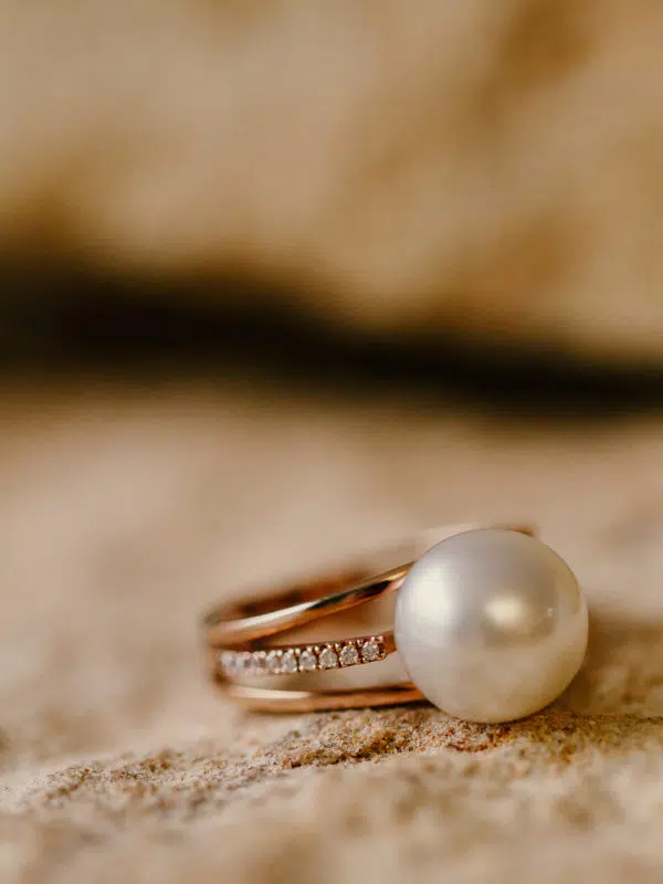 A Spinifex Ring sits on sandstone. This ring features our locally grown Australian South Sea pearl set on gold and surrounded by a myriad of white diamonds on either side of the pearl.