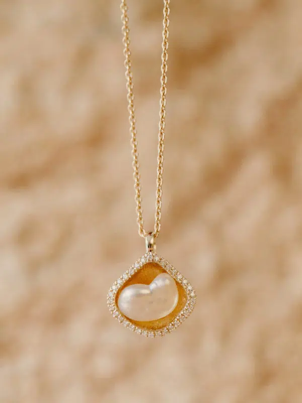 A Kimberley Lily Diamond Keshi Pearl Pendant is hung in front of a sandstone rock. This pendant features an Australian South Sea Keshi pearl, in a cup shaped like a Kimberley Lily and surrounded in a border of white diamonds. This Keshi pearl featured is an Australian South Sea Keshi pearl grown at our Cygnet Bay Pearl Farm.