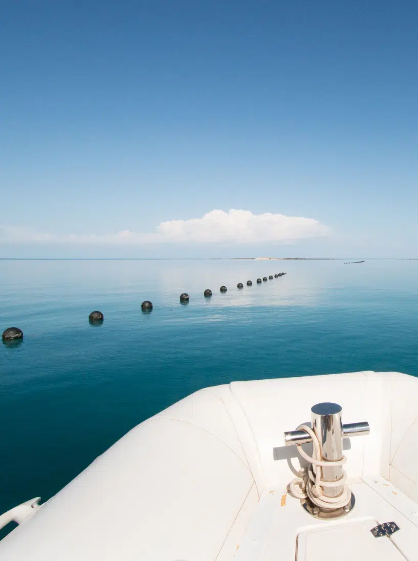A boat sits on the calm, azure waters of Cygnet Bay with the Pearl Oyster Longlines in sight. In the distance is more blue water that meets with blue skies.