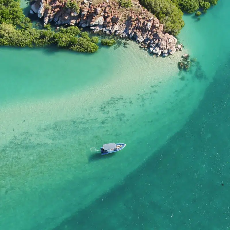 A beautiful aerial visual of a boat dancing across the waves, travelling past the Archipelago Islands that are scattered along the coastline of the Dampier Peninsula, with turquoise blue waters that are almost crystal clear.