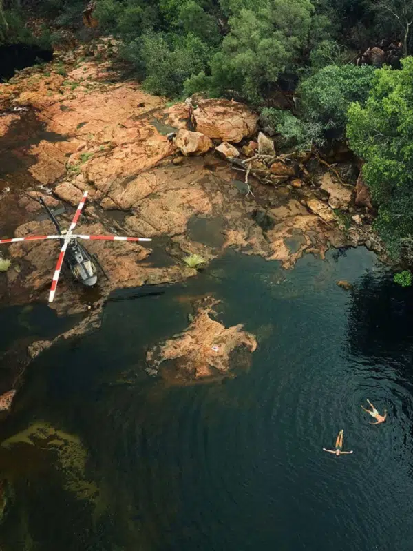 Aerial photo of a couple floating in a Kimberley gorge during a Ventur Atlas Tour. Surrounding them are beautiful lush native plants, red rock, and a helicopter that transported them to this special location.