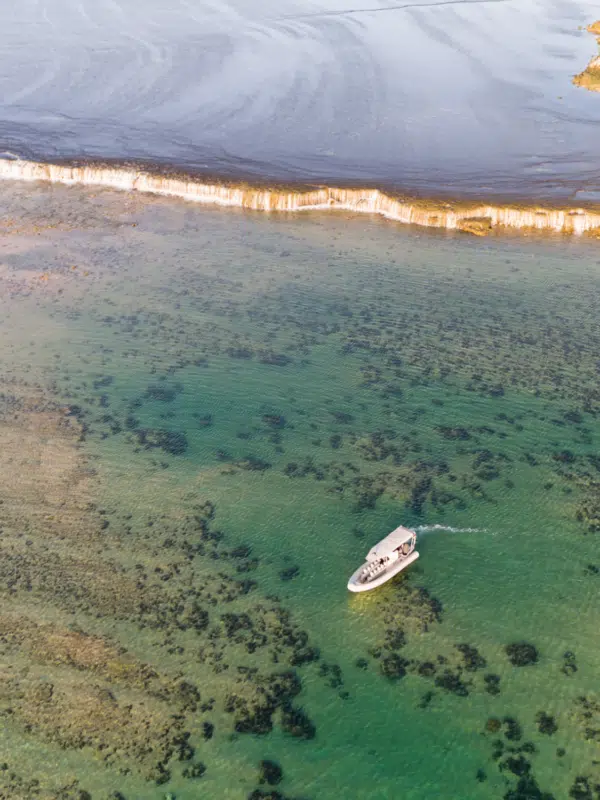 A Cygnet Bay boat sits idly next to the iconic Waterfall Reef, spilling water during the low tide of the ocean. The guests on the boat bare witness to this unique natural phenomenon and are in awe of it's cascading waterfall effect. Our Planet.